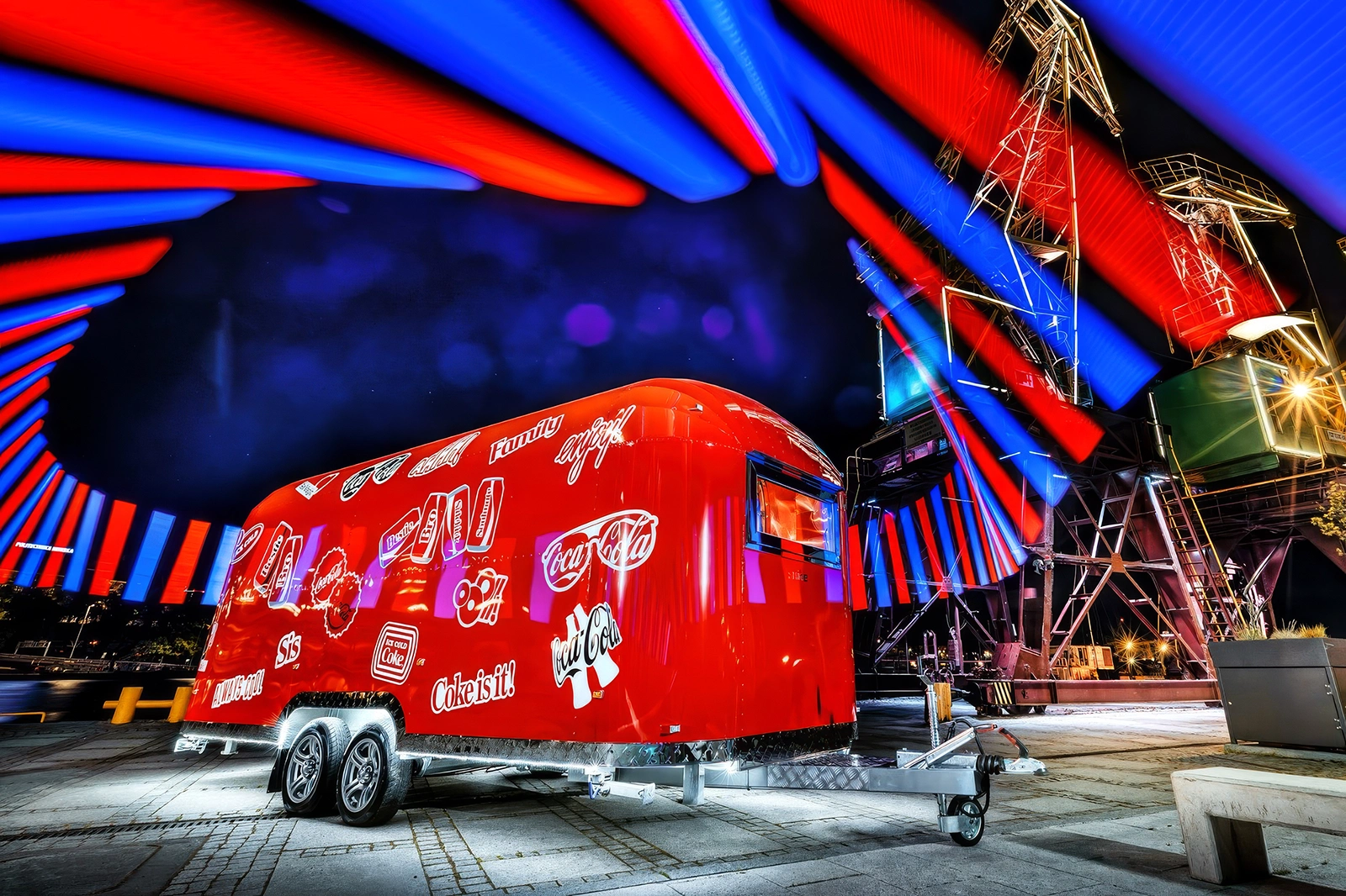 Červený reklamný príves SHINE s kompletným brandingom Coca-Cola. Luxusný mobilný showroom na pozadí nočnej industriálnej scenérie s efektnými svetelnými lúčmi.